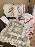 Lot displayed on a chair showing multiple items including crocheted afghans, table runner, Japanese apron, and the antique crocheted tablecloth.
