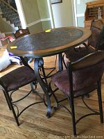 Angle view of round high top table showing wood rim, stone center, and iron leg base with chairs around it.