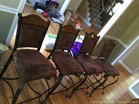 Four wood and iron dining chairs with microfiber seats and backs arranged in a row in a room.