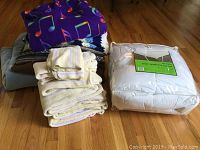 Photo of the towels, musical notes fleece throw blanket, and other blankets along with packaged XL twin mattress topper on wooden floor