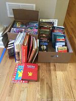 Wide view showing the boxed collection of books and media, including cookbooks, novels, Star Wars books, Pokemon books and VHS tapes