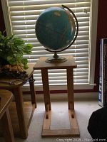 Full view of the wooden sofa table with the world globe placed on top near a window with blinds and additional furniture visible.