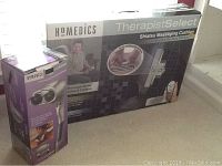 Boxed Homedics Therapist Select Shiatsu Massaging Cushion and Professional Percussion Massager shown together.
