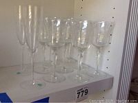 Set of 10 clear crystal stemware glasses displayed on shelf, including 2 taller flute glasses and 8 standard wine glasses.