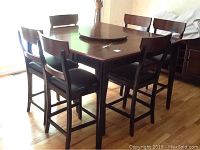 Full view of high top wood dining table with six matching chairs around it, showing overall set and wood finish.