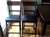 Front view of two wooden dining chairs showing dark wood frame and cushioned seats.