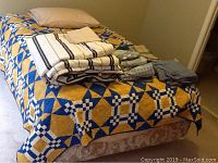 Photo of neatly made bed with quilted comforter and stack of linens on top, showing bed frame and mattress beneath.