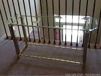 Full view of metal side table with removable glass top, showing rectangular shape and transparent glass surface reflecting light.