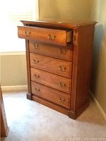 Full view photo of Bassett chest of drawers showing five drawers and brass handles, one drawer is open, placed beside a window with beige walls.