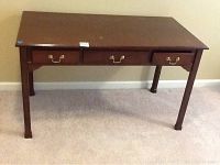 Full view of the wooden table with three drawers closed, highlighting legs and surface condition.