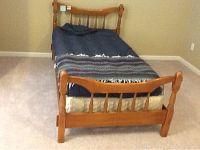 Full view of the vintage wooden twin bed frame set up with mattress and bedding in a room with beige carpet.