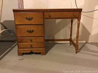 Side view of wood desk showing four drawers on left, one drawer on right and turned legs