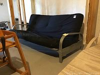 Side view of futon with black mattress and silver metal frame in basement storage area.