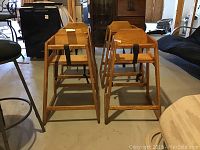 Set of four wooden high chairs, front and side view, showing natural wood finish and black seat straps with visible wear.