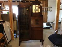 Front view showing full carved crest, curved glass display, mirror and drop-front desk
