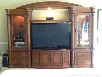 Front view of the full entertainment center showing TV, cabinet doors, drawers, and built-in lighting.