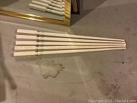 White painted wood spindles arranged on floor, showing their length and turned details