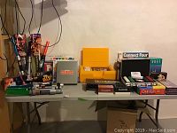 Overview of the lot showing games and five Star Wars electronic light sabers on a table against a plain wall. Boxed board games including Scruples, Trouble, Pictionary, Texas Hold Em, Cranium and Connect Four are visible.