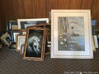 Photo showing multiple framed artworks arranged on floor against wall.
