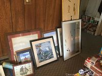 Several coastal themed framed prints arranged on floor against wood paneling. Includes sailboats, lighthouses and birds in flight.
