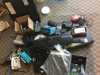 Lot of assorted electronics and accessories including Magnavox radio/tape player, Sony VHS recorder, remotes, and power cords on carpet