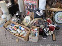 Wide view showing the beer cans in cardboard boxes, multiple beer signs including a Budweiser framed sign, various beer memorabilia items including stein-shaped ice bucket, tap handle and small figurines.