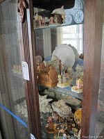Glass cabinet shelf with various porcelain figurines, including Precious Moments, Hummel and others