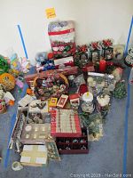 Overview of various Christmas decorations on the floor including wreaths, ceramic trees, ornaments, boxed items and battery operated candles.