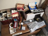 Multiple boxes and trays containing assorted rings, watches, lighter in open layout on table
