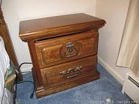 Photo of one nightstand showing two drawers with brass handles and medium brown wood finish.