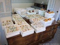 Multiple styrofoam trays on dresser and bed showing rows of Precious Moments porcelain hanging ornaments and three Peanuts pumpkin head figurines