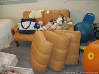 Full view of tan leather sofa with three extra seat cushions in front, several dolls and a bag placed on the seating area.