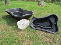 View of the two black plastic yard ponds and white container on grass with pond pump tubing visible.