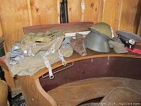Photo showing East German steel helmet, military peaked cap, camouflage bags, belt, and holster on a wooden bench.