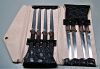 Six steak knives with wooden handles secured inside black textured folding case open to show blades.