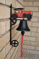 Side view of cast iron bell mounted on bracket with red vintage car and red pull cord, showing the bell and portion of the wall.