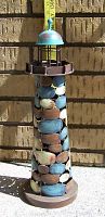 Front view of large metal lighthouse candle holder outdoors with tape measure showing height approximately 18.5 inches.