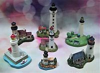 Seven vintage lighthouse replicas arranged on a surface with colored background. Shows overall collection size, detail, and condition.