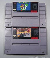 Front view of two Super Nintendo game cartridges, Super Mario World above and F-Zero below, showing vintage label art and cartridge condition.