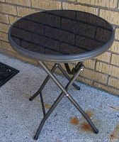 Side view of the round patio table showing the black tempered glass top and metal frame