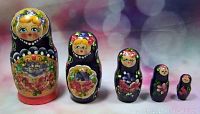 Five handcrafted Russian Matryoshka nesting dolls displayed in descending order front view showing detailed hand-painted faces, floral designs, and colorful headscarves on a blurred light background.