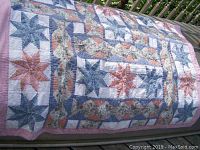 Full view of quilt spread out showing star pattern and pink checked border.