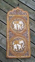 Full view of the rectangular sequined elephant wall hanging on a deck surface, showing two white elephant motifs within circular borders on a brown fabric.