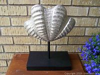 Front view of heavy metal shell decor on black stand showing detailed texture and shape.