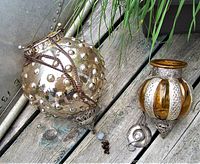 Two vintage hanging lanterns placed on a wooden surface surrounded by grass, showing their shape, metal chains, and detailing including oxidation on the larger lantern.