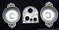 Two pewter porringers with decorative scrollwork handles flank Henry Penny's pasta measure featuring a chicken design and pasta size holes.