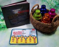 Vintage woven basket with four shiny martini shakers in blue, green, orange, and purple, along with the martini recipe book and sealed Drinking Buddies markers pack.