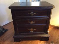 Front view of dark wood side table chest with three drawers and brass handles