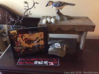 Photo of Dale Earnhardt memorabilia including the wall clock, baseball cap, bumper sticker, the wooden stool with ceramic birds and metal jewelry tree on and beside it.