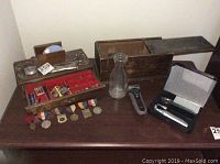 Top view of table with vintage grooming tools, medals, wooden boxes, glass milk bottle, and electric shaver.